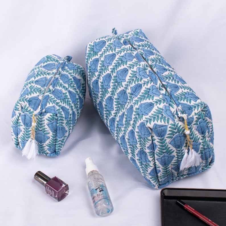 May include: Two blue and white floral print zippered pouches with white tassels. The larger pouch is on the right and the smaller pouch is on the left. The pouches are on a white surface.