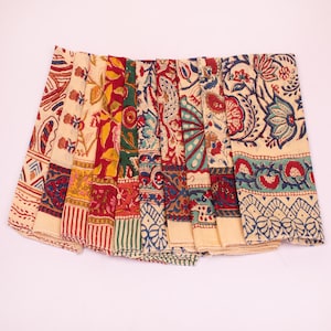 May include: A collection of folded fabric napkins featuring a cream-colored base with intricate block-printed floral and geometric patterns in shades of red, green, yellow, and blue, arranged in a fan-like display showing various textile designs.