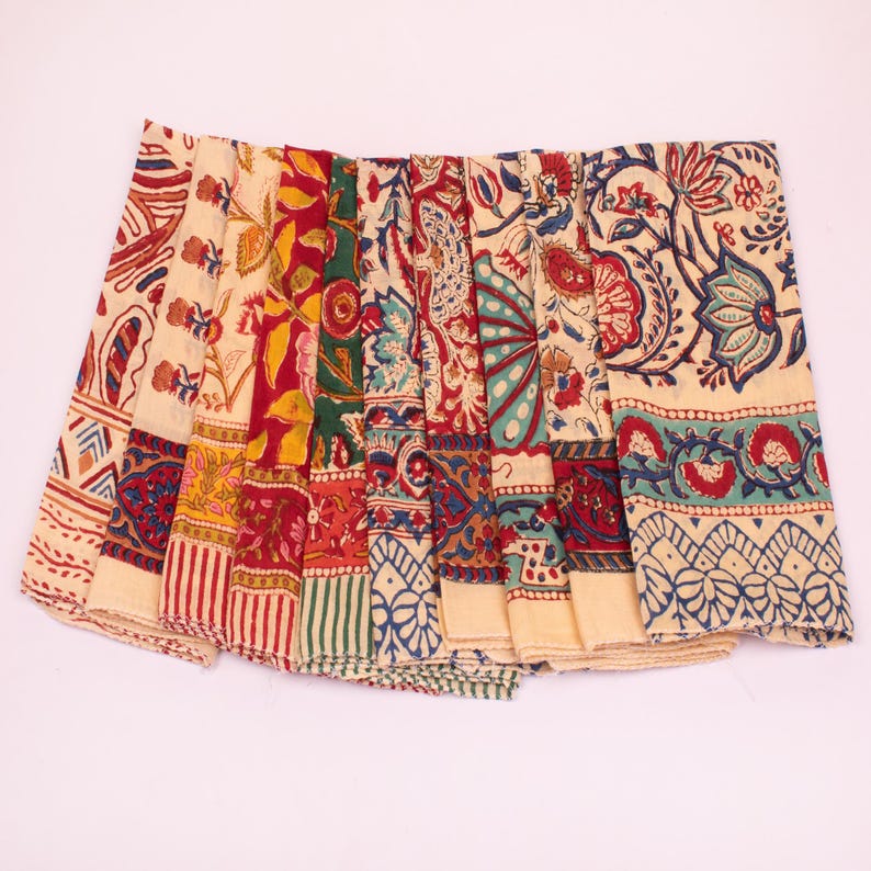 May include: A collection of folded fabric napkins featuring a cream-colored base with intricate block-printed floral and geometric patterns in shades of red, green, yellow, and blue, arranged in a fan-like display showing various textile designs.