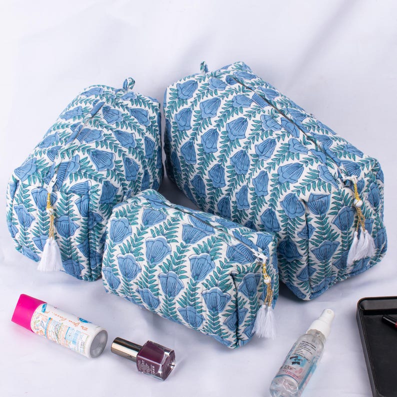 May include: Three blue and white floral print zippered pouches with white tassels. The pouches are different sizes and are arranged on a white surface.