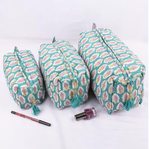 May include: Three teal cosmetic bags with a paisley pattern in pink and white. Each bag has a zipper closure and a teal tassel. A red eyeliner pencil and a bottle of purple nail polish are also in the image.