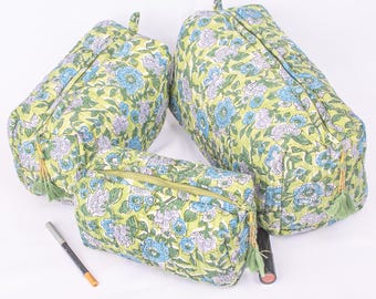 May include: Three quilted cosmetic bags with a floral pattern in shades of green, blue, and white. The bags have a zippered closure and a tassel. A black eyeliner pencil and a lipstick are next to the bags.