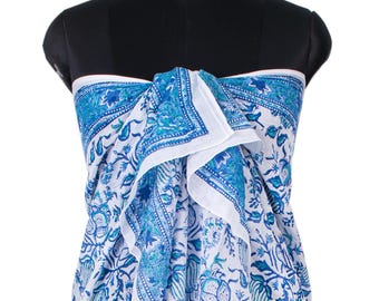 May include: A white sarong featuring a repeating floral pattern in shades of blue and turquoise. The fabric is draped around a black mannequin, showcasing a detailed botanical print with intricate leaves and blossoms across the entire surface.
