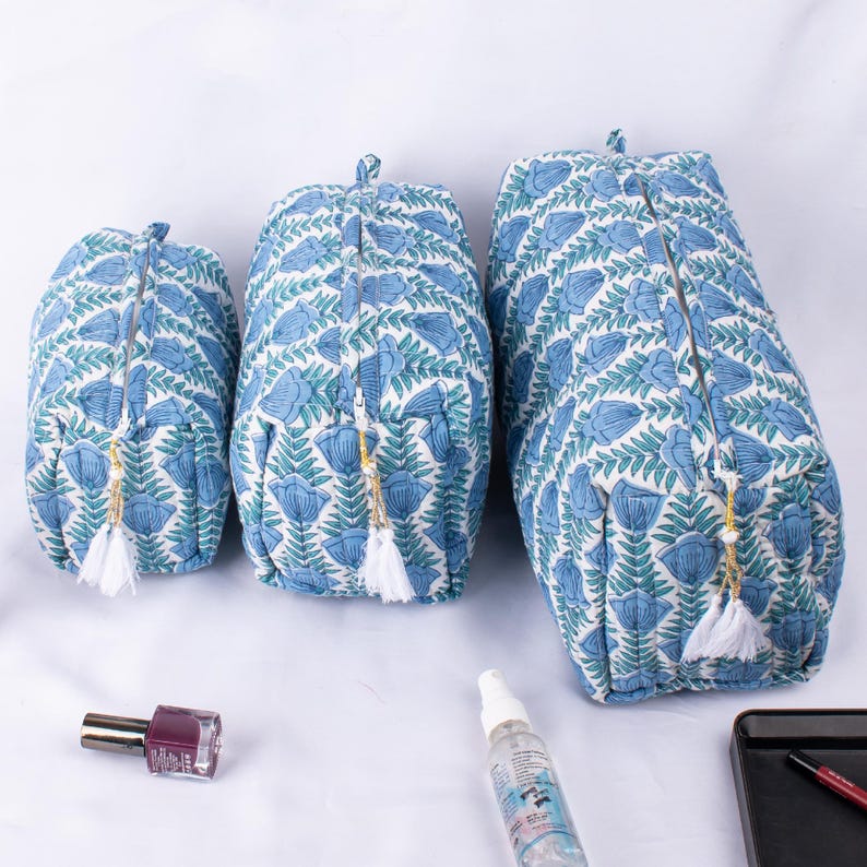 May include: Three blue and white floral print zippered pouches with white tassels. The pouches are different sizes and are arranged from largest to smallest.