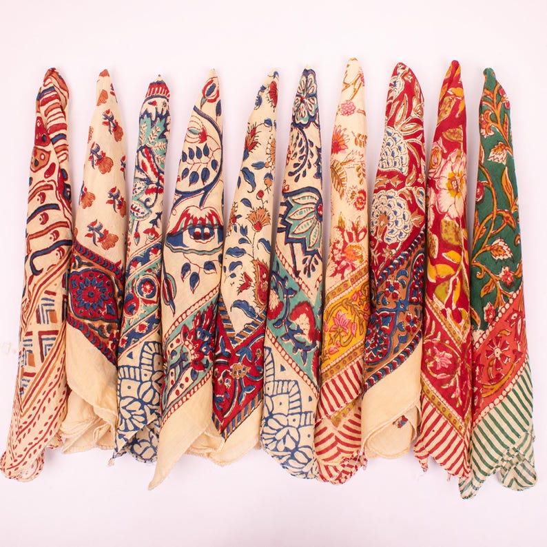 May include: A collection of ten folded cotton bandanas arranged in a row, each featuring distinct block-printed patterns in vibrant colors including red, blue, green, yellow, and cream, showcasing intricate floral, geometric, and paisley motifs.