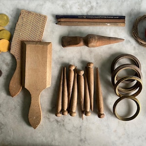 Può includere: Una collezione di oggetti vintage che include gettoni circolari gialli, due palette in legno, tre matite, un attrezzo in legno, un uovo rosso in un nido, tre chiavi in metallo, sette pioli in legno, tre anelli in metallo e una rotella.