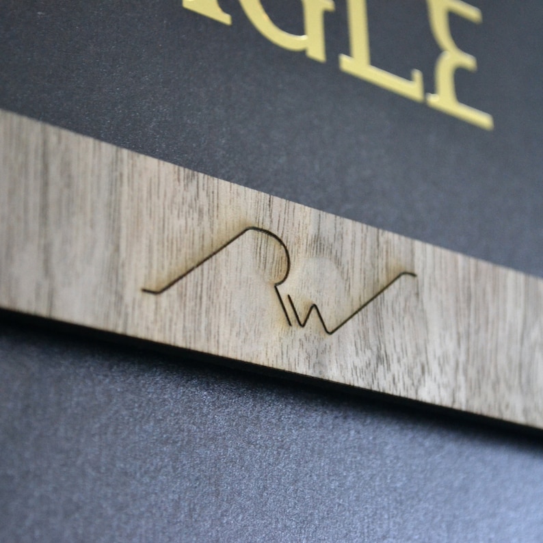 May include: A close-up of a wooden sign with the text "Eagle" in gold lettering and a stylized wave design with the letters "RW" inside the wave.