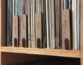 May include: A wooden shelf with vinyl records organized by genre. The genres are labeled with wooden tags: Jazz, Rock, Pop, and Electronic.