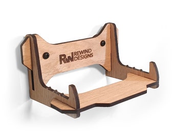 May include: Wooden wall mount for a video game console, with the logo "RW Rewind Designs" engraved on the front. The mount has a shelf for controllers or other accessories.