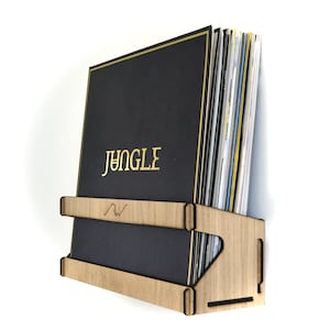 May include: A wooden record shelf with a black vinyl record with the word "JUNGLE" in gold lettering. The shelf is designed to hold multiple records.