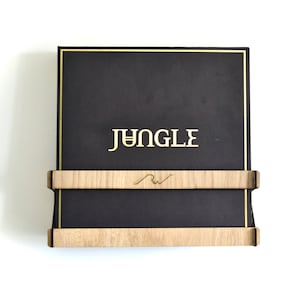 May include: A black vinyl record with a gold border and the word "JUNGLE" printed in gold letters. The record is displayed on a wooden wall mount with a small logo.