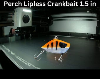 May include: A Perch Lipless Crankbait, 1.5 inches long, with orange, black, and silver details. The fishing lure has two treble hooks and is designed for 3D printing. The text "STL + 3MF | Digital File For 3D Printing" is visible.