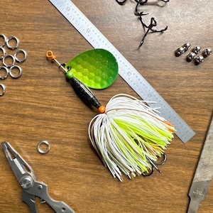May include: A green and black fishing lure with white and yellow feathers. The lure has an orange bead and a silver hook.