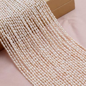 May include: Strands of creamy white, oval-shaped pearls. The pearls are strung together, creating a flowing, textured appearance. The pearls are a soft, off-white color, and the image is well-lit, highlighting the natural luster of the pearls. The pearls are likely for jewelry making.