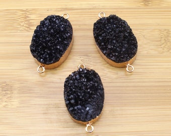 May include: Three black oval-shaped agate gemstone pendants with gold-toned metal connector loops. The pendants have a rough, textured surface.