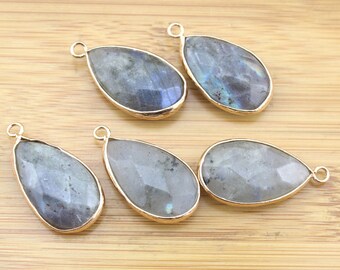 May include: Five teardrop-shaped labradorite gemstone pendants with gold-toned metal bail loops. The stones are a mix of gray, blue, and black with iridescent flashes.