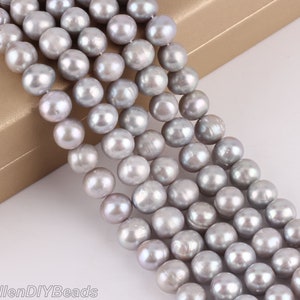 Könnte beinhalten: Eine Strähne grauer Perlen. Die Perlen sind rund und glatt und auf einem durchsichtigen Faden aufgefädelt. Die Perlen sind alle ungefähr gleich groß.