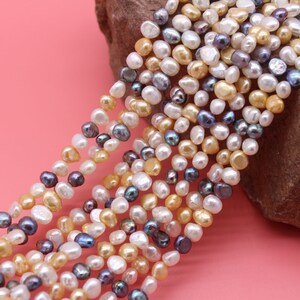 May include: A strand of mixed-color freshwater pearls. The pearls are a mix of white, cream, and gray. The pearls are irregular in shape and have a slightly iridescent sheen.
