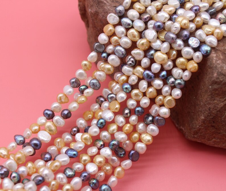 May include: A strand of mixed-color freshwater pearls. The pearls are a mix of white, cream, and gray. The pearls are irregular in shape and have a slightly iridescent sheen.