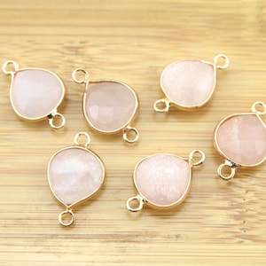 May include: Six gold-tone teardrop-shaped charms with a white, sparkly finish. Each charm has two jump rings for attaching to jewelry.