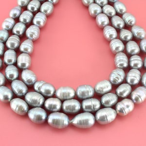 Könnte beinhalten: Eine Kette aus grauen Perlen, mit drei Reihen Perlen, auf einem rosa Hintergrund.