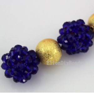 Puede incluir: Primer plano de un collar hecho con cuentas doradas y azules. Las cuentas azules son facetadas y se agrupan, creando una forma de flor. Las cuentas doradas son redondas y tienen una superficie texturizada.