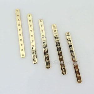 May include: Five gold metal strips with multiple holes. The strips are different lengths and are arranged in a row from longest to shortest.