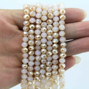 May include: A strand of faceted glass beads in a light champagne color. The beads are round and have a slight iridescent sheen.