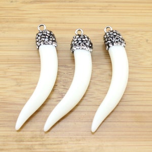 May include: Three white tooth-shaped pendants with silver tops adorned with clear rhinestones.