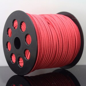 Può includere: Un rotolo di cordoncino in pelle scamosciata rosso avvolto attorno a un rotolo di plastica nero. Il cordoncino è largo circa 3 mm.