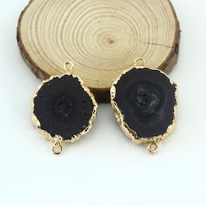 May include: Two black agate slices with gold-toned edges and jump rings. The agate slices are round and have a natural, irregular shape.