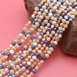 May include: A strand of mixed-color freshwater pearls. The pearls are a mix of white, cream, and gray. The pearls are irregular in shape and size.