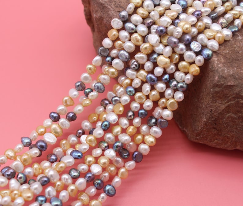 May include: A strand of mixed-color freshwater pearls. The pearls are a mix of white, cream, and gray. The pearls are irregular in shape and size.