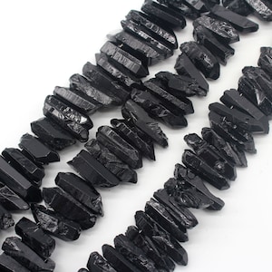 Puede incluir: Puntos de cristal de cuarzo negro en bruto, también conocidos como turmalina negra, dispuestos en dos filas. Los puntos son ásperos y dentados, con un acabado natural sin pulir.