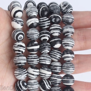 May include: A strand of round beads with a black and white striped pattern. The beads are spherical and appear to be made of stone or a similar material. The alternating black and white stripes create a bold, graphic design.