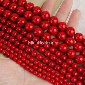 May include: A strand of red coral beads in various sizes. The beads are round and smooth, with a glossy finish. The beads are arranged in a graduated pattern, with the largest beads at the top and the smallest beads at the bottom.