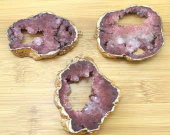 May include: Three pink agate slices with gold-plated edges. Each slice has a natural hole in the center. The slices are arranged on a wooden surface.