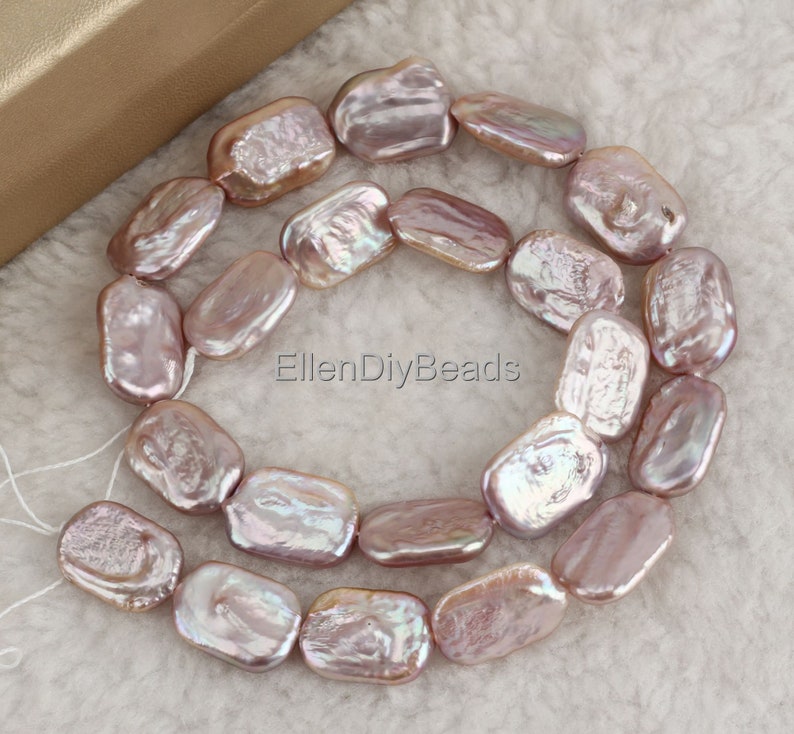 May include: A strand of iridescent pink freshwater pearls, each pearl is a unique, irregular oval shape. The pearls are strung on a white thread and are ready to be used for jewelry making.