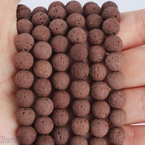 May include: A strand of dark brown lava rock beads. Each bead is round with a porous texture and is approximately 8mm in diameter. The beads are strung together, ready for jewellery making. The beads are held in a hand.