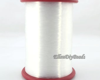 May include: A spool of clear elastic thread wound around a red plastic bobbin. The thread is used for jewelry making and beading.