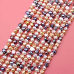 May include: A strand of mixed color freshwater pearls. The pearls are a variety of shapes and sizes, including round, oval, and baroque. The pearls are a mix of white, cream, and gold.
