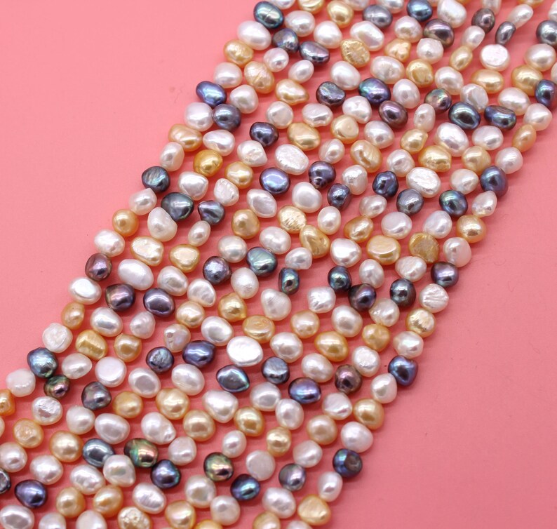 May include: A strand of mixed color freshwater pearls. The pearls are a variety of shapes and sizes, including round, oval, and baroque. The pearls are a mix of white, cream, and gold.
