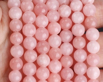 Puede incluir: Una hebra de cuentas redondas de color rosa pálido hechas de piedra natural. Las cuentas son lisas y pulidas, con una apariencia ligeramente translúcida.