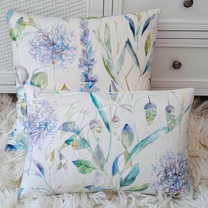 May include: Two decorative throw pillows with a watercolour floral pattern. The pillows feature a white background with blue, green and yellow flowers and leaves.
