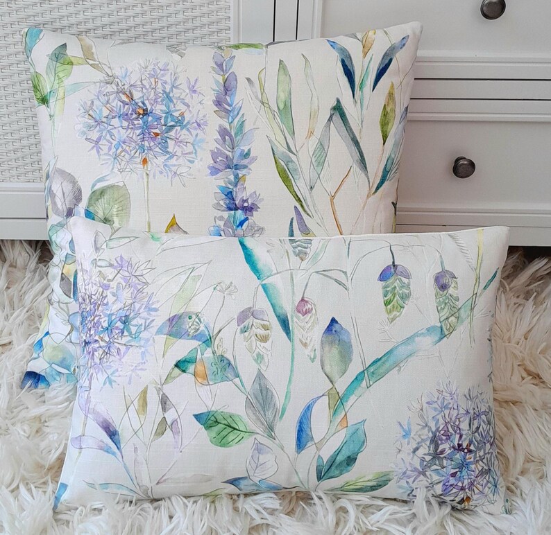 May include: Two decorative throw pillows with a watercolour floral pattern. The pillows feature a white background with blue, green and yellow flowers and leaves.