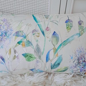 May include: A white cushion with a watercolour design of blue, green and purple flowers and leaves.
