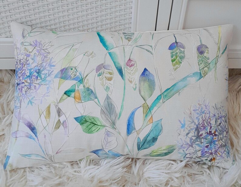 May include: A white cushion with a watercolour design of blue, green and purple flowers and leaves.