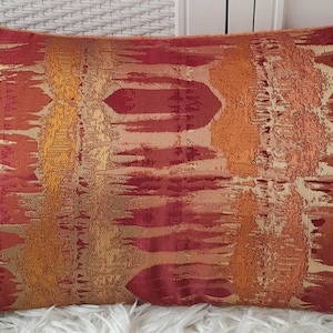 May include: A decorative cushion with an abstract pattern in shades of red, orange, and gold. The cushion has a textured fabric with a subtle sheen.