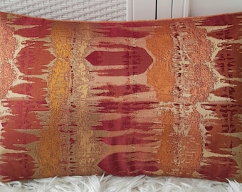 May include: A decorative throw pillow with an abstract pattern in shades of red, orange, and gold. The pillow has a textured fabric with a subtle sheen.