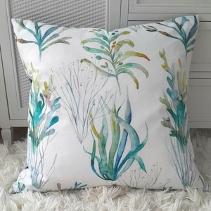May include: A white cushion with a watercolour design of blue, green and yellow seaweed. The cushion is ideal for adding a touch of nature to any room.